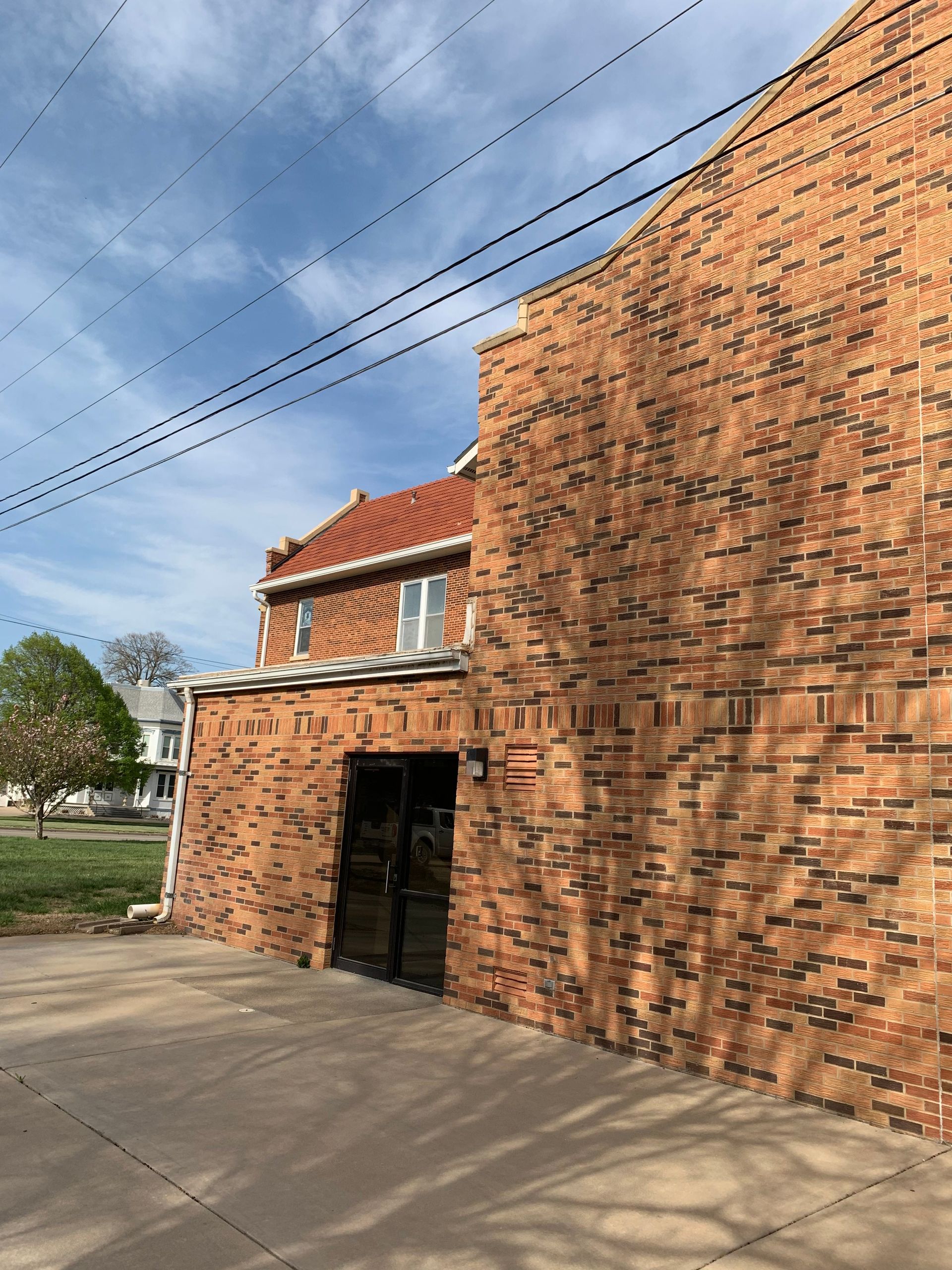 Brick building exterior with door, red tile roof, and power lines against a blue sky.