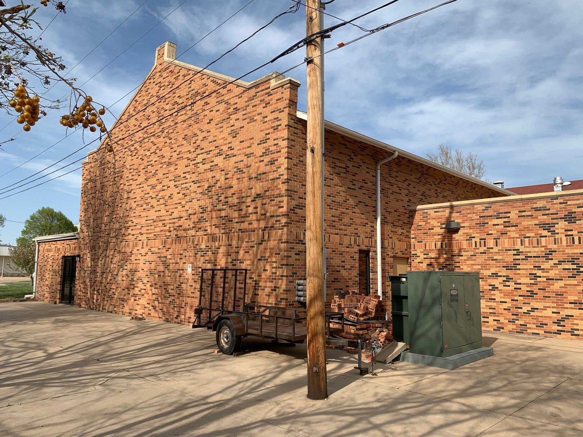 Red brick building with a utility box, trailer, and utility pole. Sunny, daytime setting.