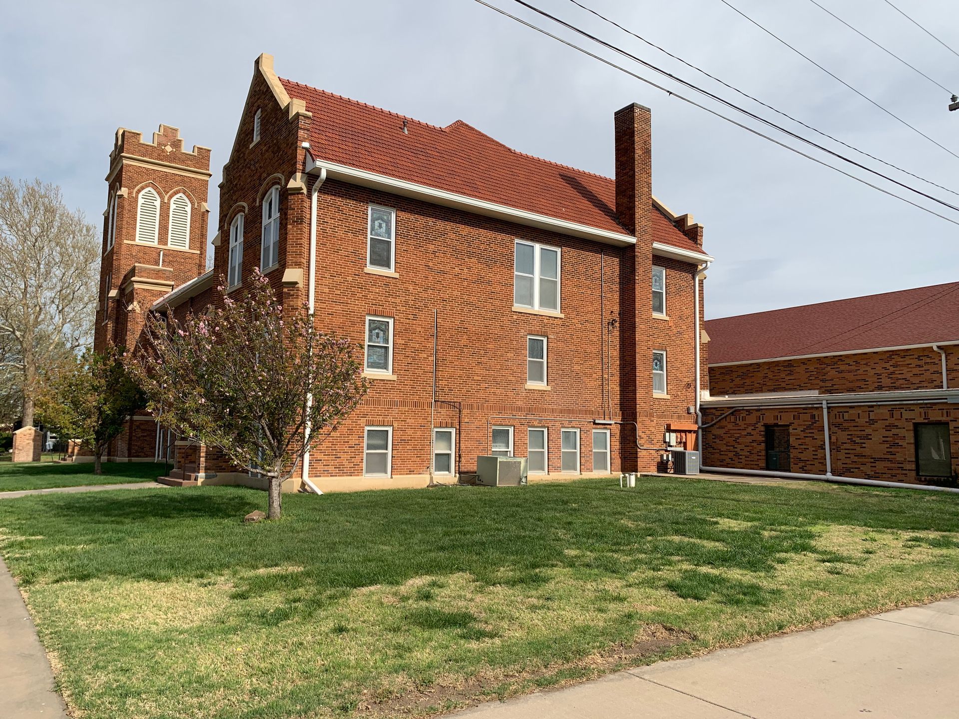 Brick church building with a red tile roof and a tower; green grass lawn.