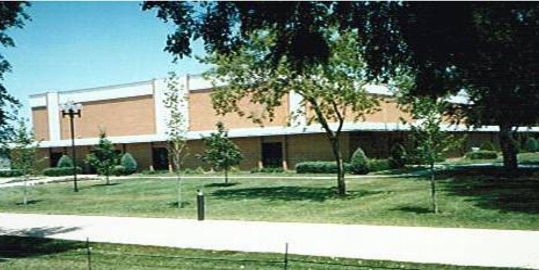 Building with a red brick facade, set among green trees and a grassy lawn.