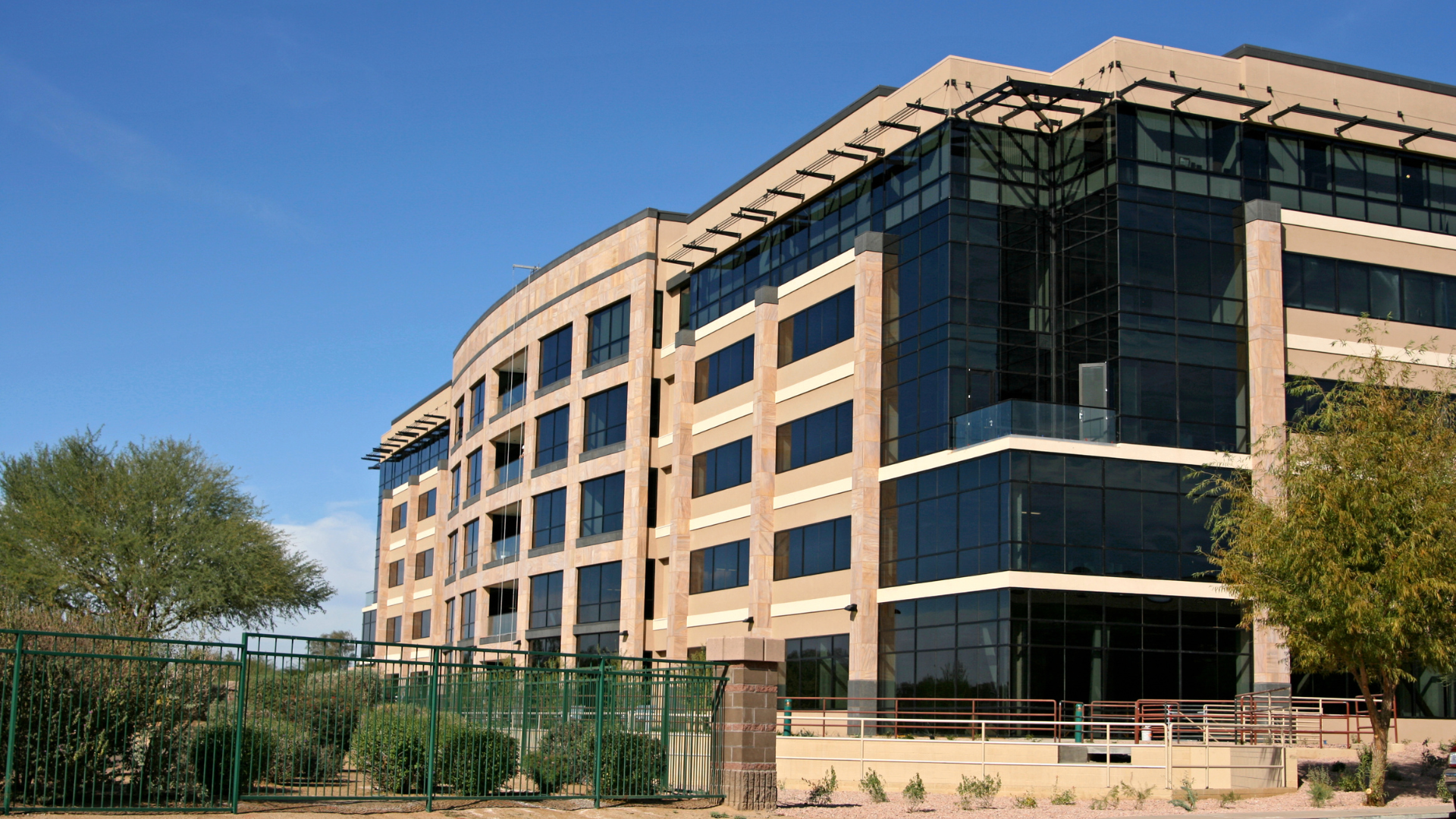 Multi-story office building with dark glass windows and beige exterior under a blue sky.