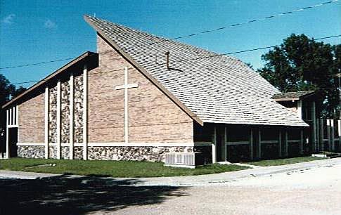 Brick church building with slanted roof and cross. Exterior view.
