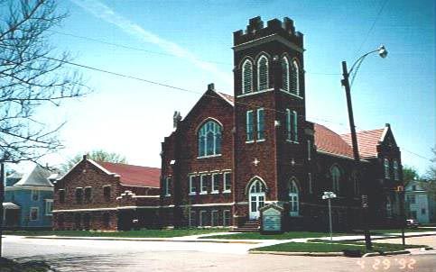 Brick church with tower, arched windows, and a red roof, on a sunny day.