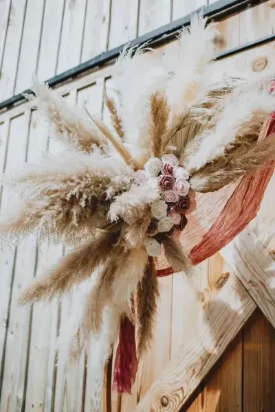 Rustic dried pampas grass wreath with pink flowers on a light wood wall