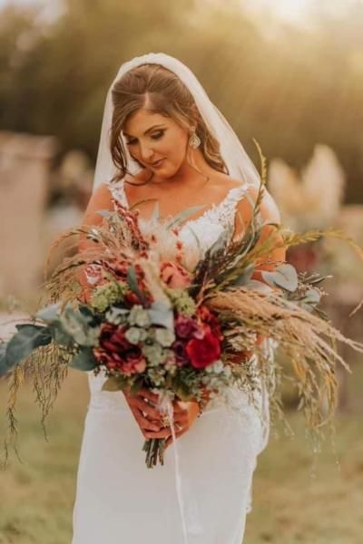 Bride in a white gown holding a large bouquet of red, pink, and green flowers outdoors