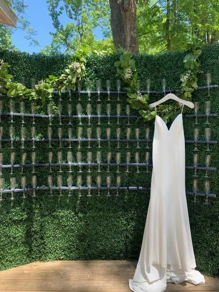 White sleeveless dress on a hanger before a green hedge and blue sky outdoors