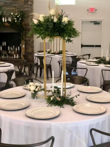 Round banquet table with white linens, plates, candles, and green floral centerpiece in a reception hall