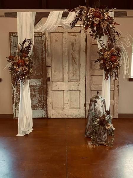Rustic wedding arch with white drapes and fall floral arrangements in front of antique doors