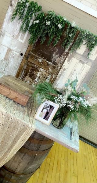 Rustic table display with green foliage, a framed photo, and a wooden barrel in a decorated indoor setting