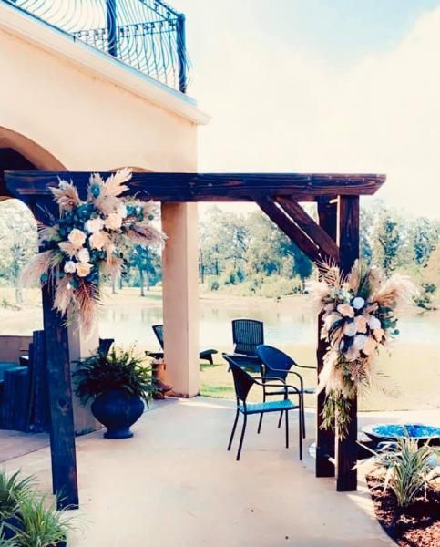 Decorated wooden pergola on a patio with floral arrangements and a chair under a bright blue sky