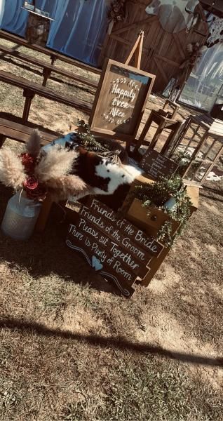 Rustic outdoor display with a chalkboard sign, potted flowers, and a black-and-white dog statue or plush.