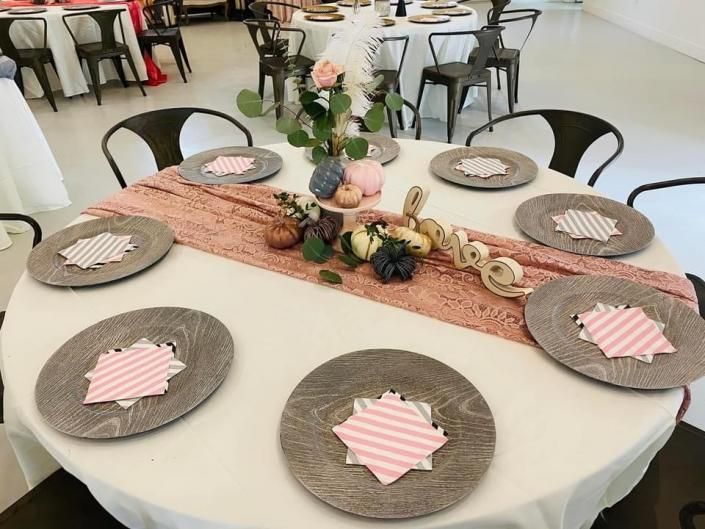Round table set with woven placemats, pink napkins, and a floral centerpiece in a bright dining hall