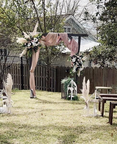 Outdoor wedding arch with pink drapes and white floral arrangements in a grassy backyard