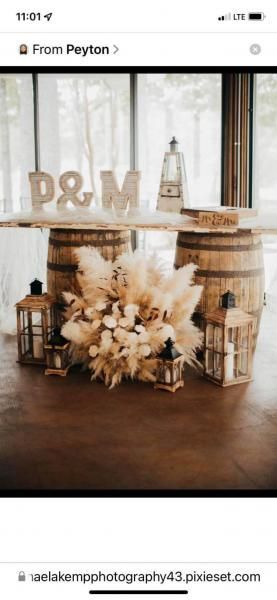 Rustic wedding decor with wooden barrels, dried flowers, and large gold “P&M” initials by windows