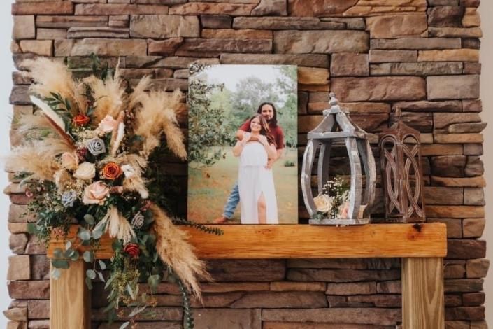Decorated stone mantel with floral arrangement, framed couple photo, lantern, and rustic wooden decor