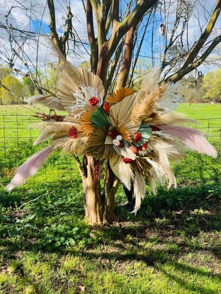 Decorative feathered floral arrangement hanging on a tree in a grassy park