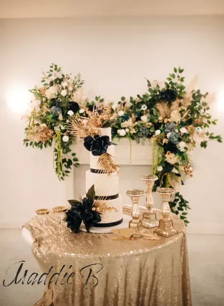 Elegant white-and-gold cake table with floral arrangements and glassware for a celebration
