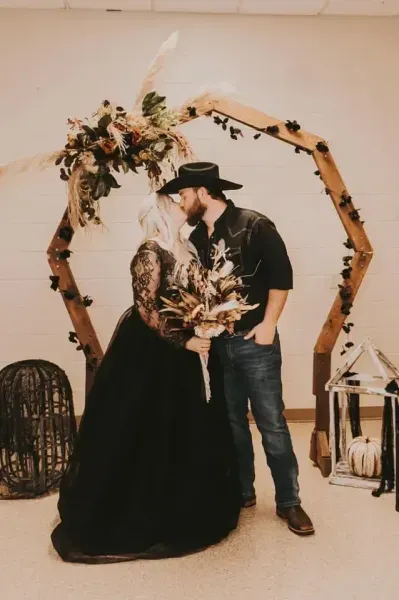 Couple posing under a floral wooden arch, holding hands in a rustic indoor wedding setting