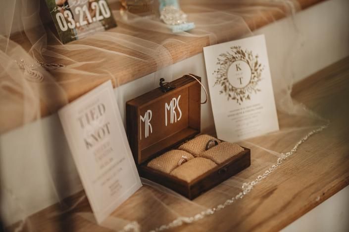 Wedding rings in a wooden box with “Mr & Mrs” engraving, beside a card on a table
