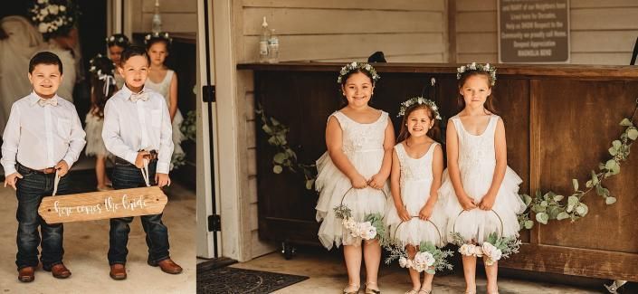 Two children hold a sign, beside three flower-garlanded girls sitting on stools in a decorated entryway.
