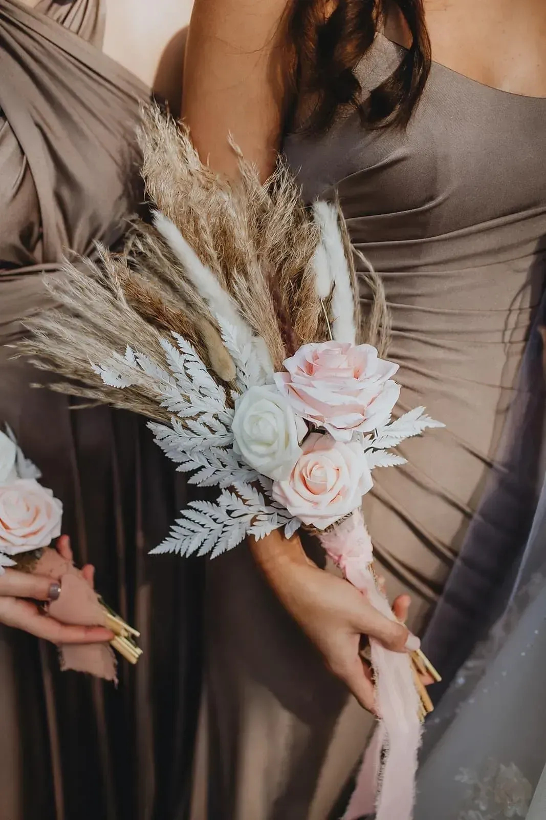 Bridesmaids holding neutral-toned bouquets with pink roses and dried grasses in taupe dresses