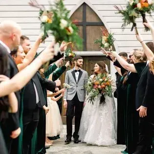 Wedding couple walking through raised flower archway with guests on both sides holding bouquets