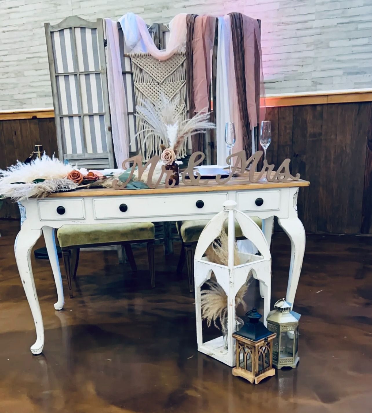 Rustic white desk with boho decor, macramé wall hanging, lanterns, and feathers in a room with wood paneling