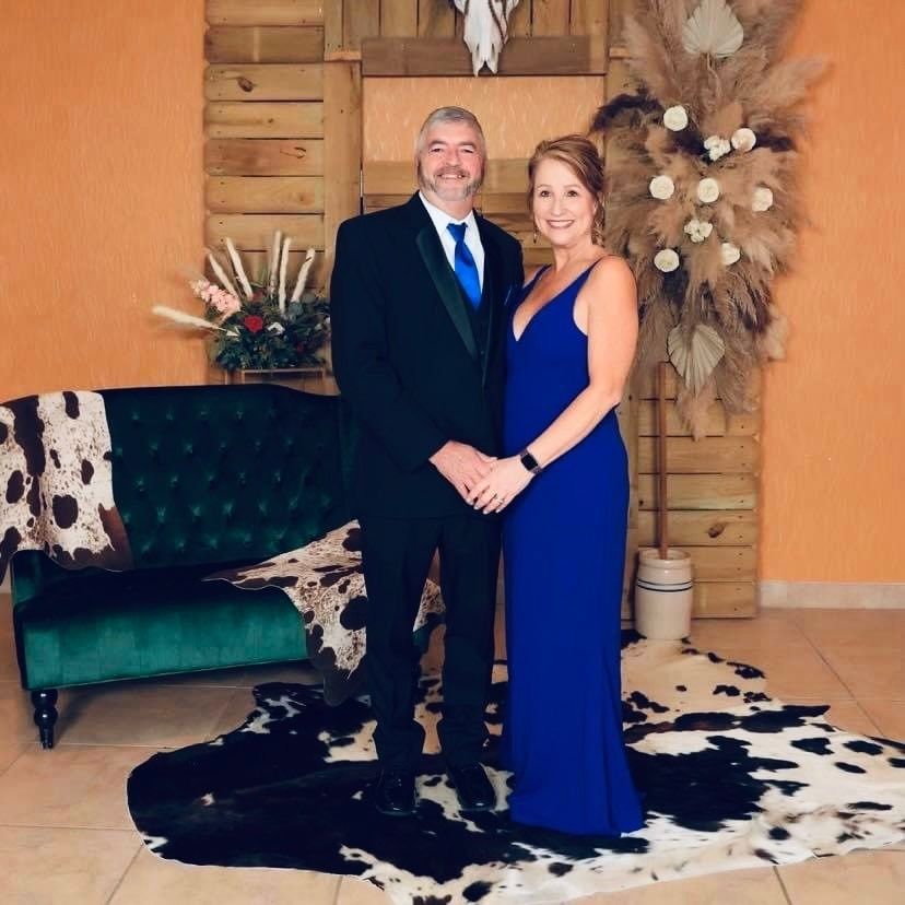Couple posing in formal attire on a rustic set with cowhide rug and floral decor