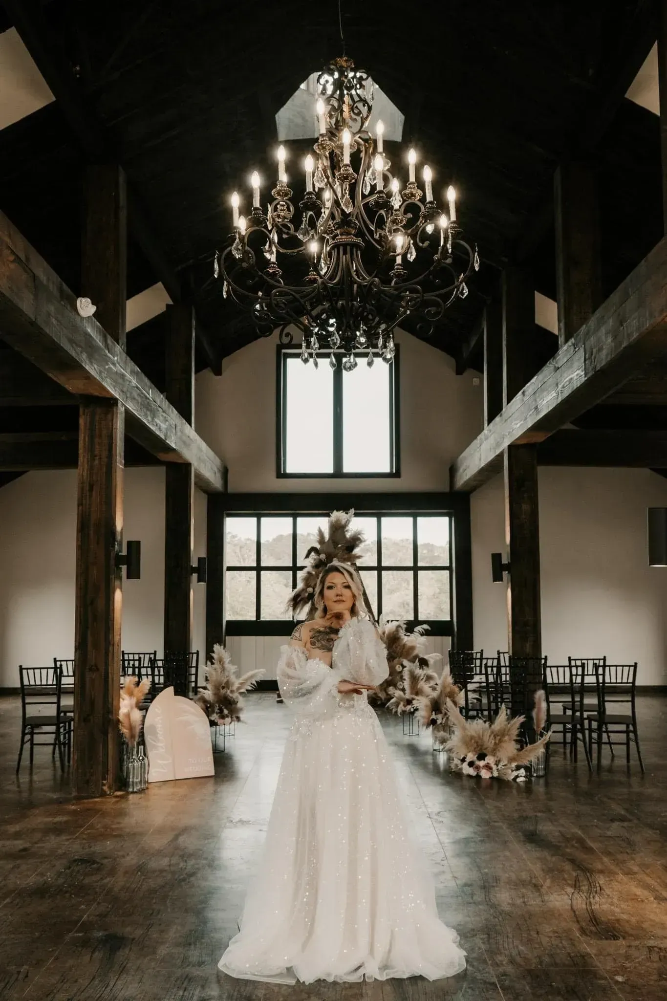 Bride in a white gown standing in a dark, elegant hall beneath a large chandelier