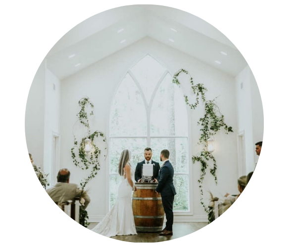 Wedding ceremony in a bright white chapel, with a couple and officiant beside a wooden barrel altar.
