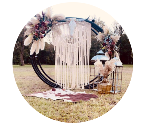 Outdoor wedding arch with black circular frame, white drapes, and floral arrangements on a grassy lawn