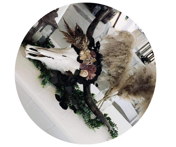 Decorative deer skull with flowers and greenery on a white tabletop, surrounded by dried plants