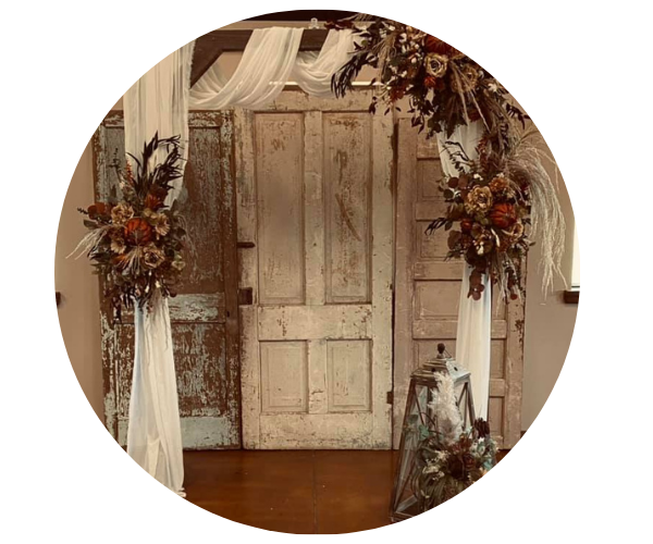 Rustic wooden door framed by white drapes and dried floral arrangements on a warm-toned floor