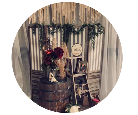 Rustic wedding display with barrel, flowers, ladder, greenery garland, and framed photos on draped backdrop