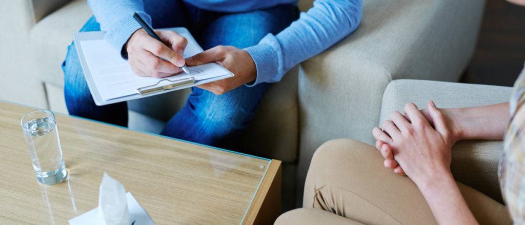 A man is writing on a clipboard while sitting next to a woman on a couch. Participating in Catholic Counseling in Texas.