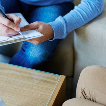 A person is sitting on a couch writing on a clipboard. During a Catholic counseling session in Grapevine Texas.