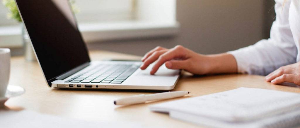 A person is typing on a laptop computer at a desk participating in online Catholic Counseling in Texas.