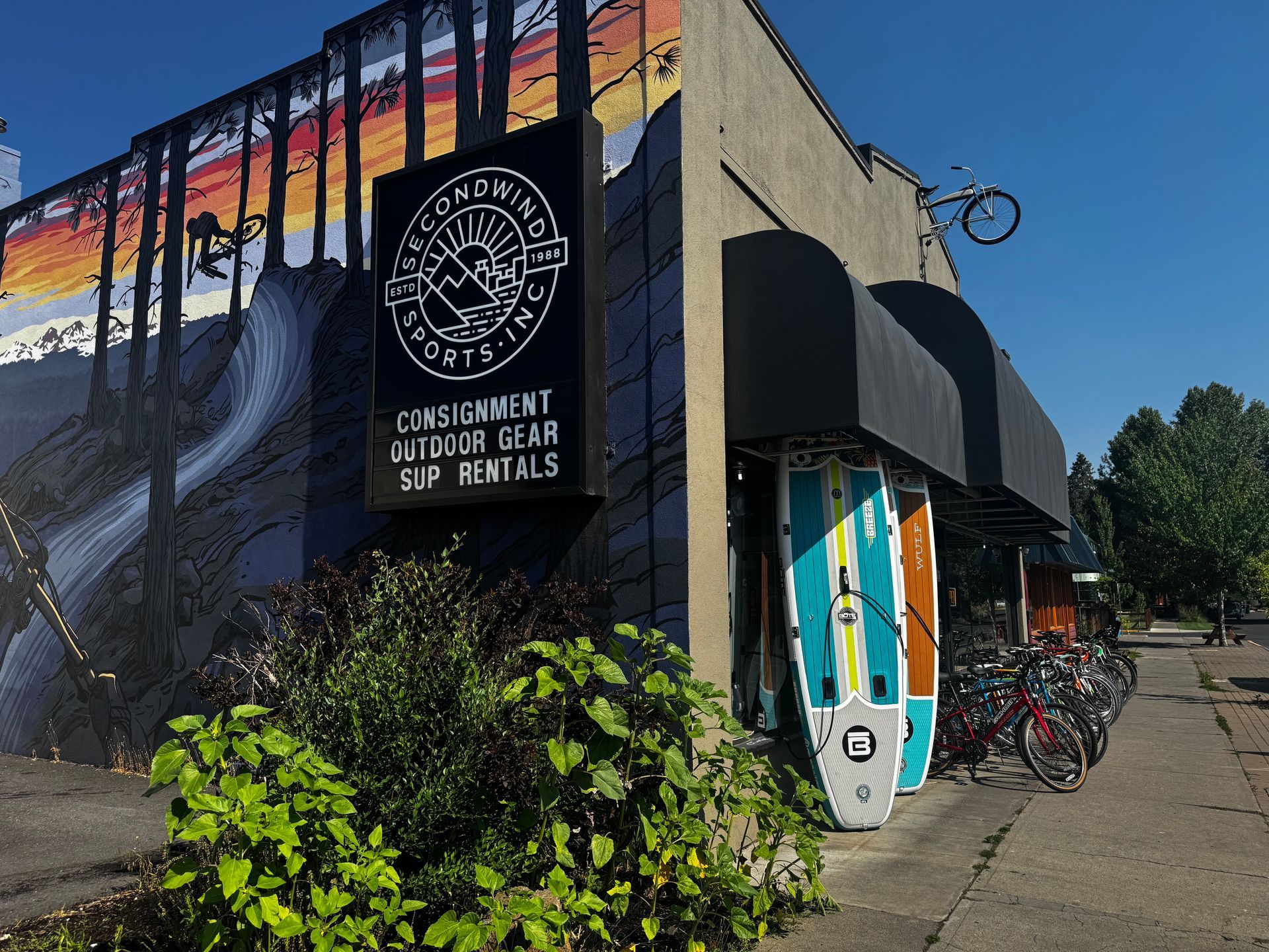 Corner building with mural, sign reading “Consignment Craft Sales,” and bicycles parked outside.