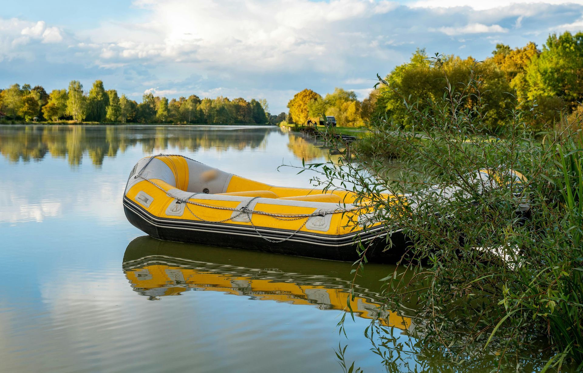 Yellow inflatable boat on a calm lake with trees and blue sky reflected in the water