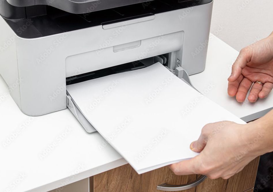 Person removing a stack of printed white paper from a gray and black printer.