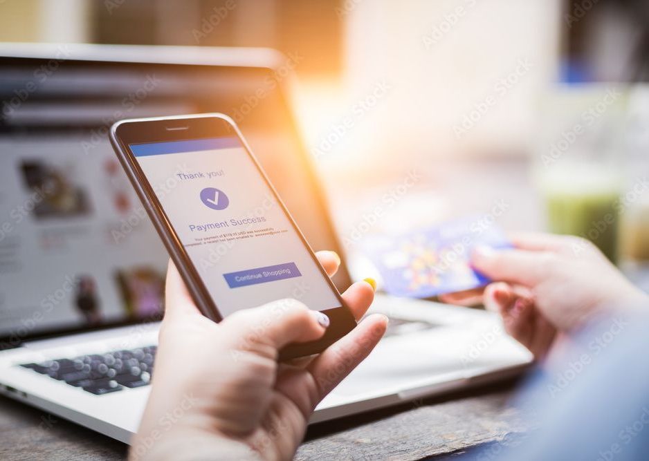 Person holding phone and credit card, shopping online with a laptop.