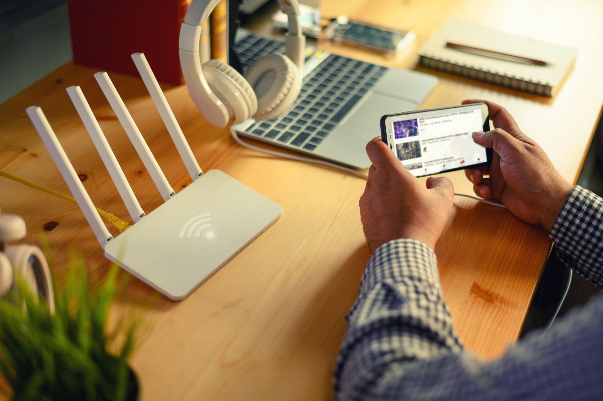Person using a phone, router, laptop, and headphones on a desk; listening to music.