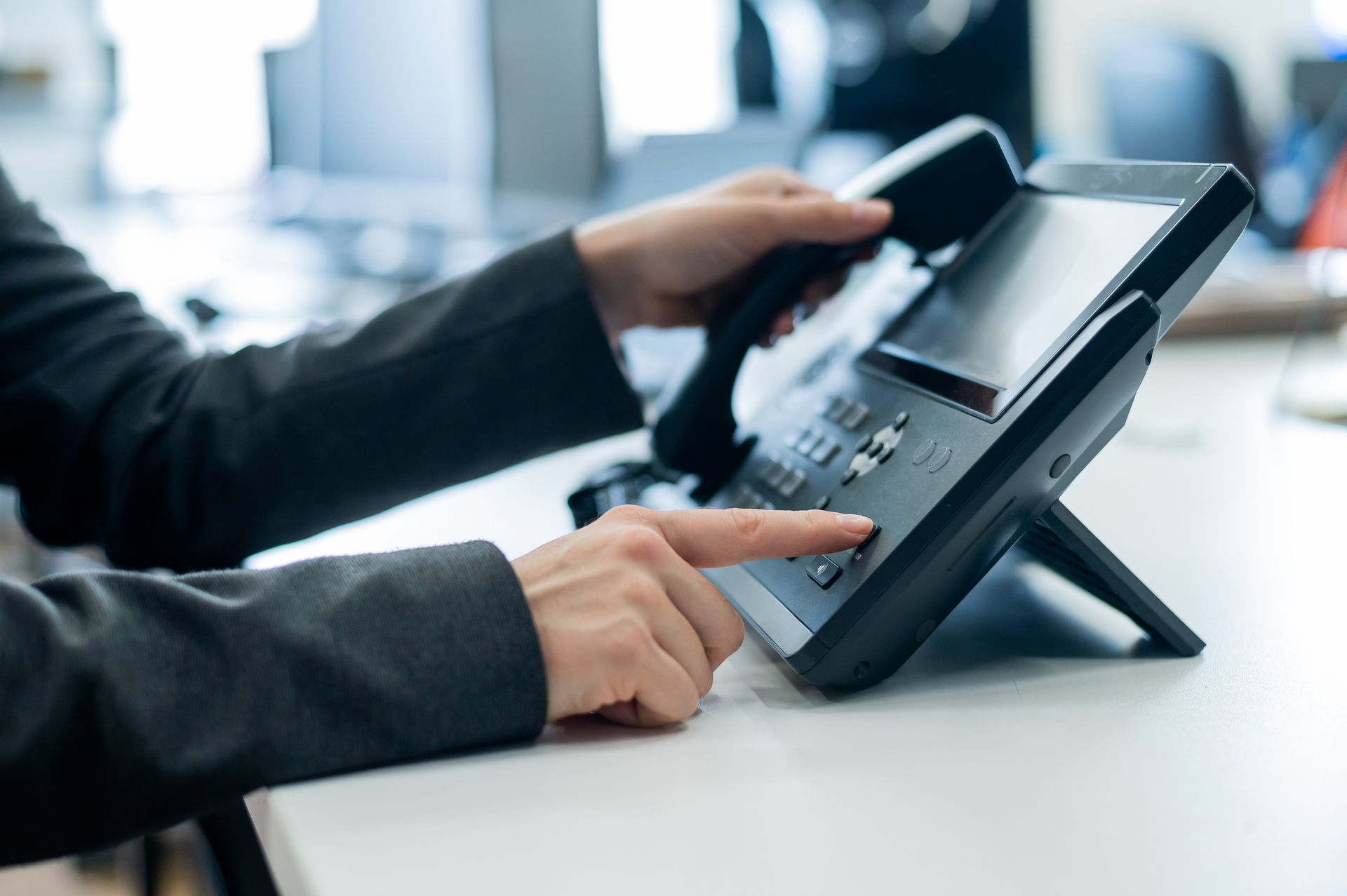 Person in suit dials a number on a modern office phone with a large screen, likely making a call.