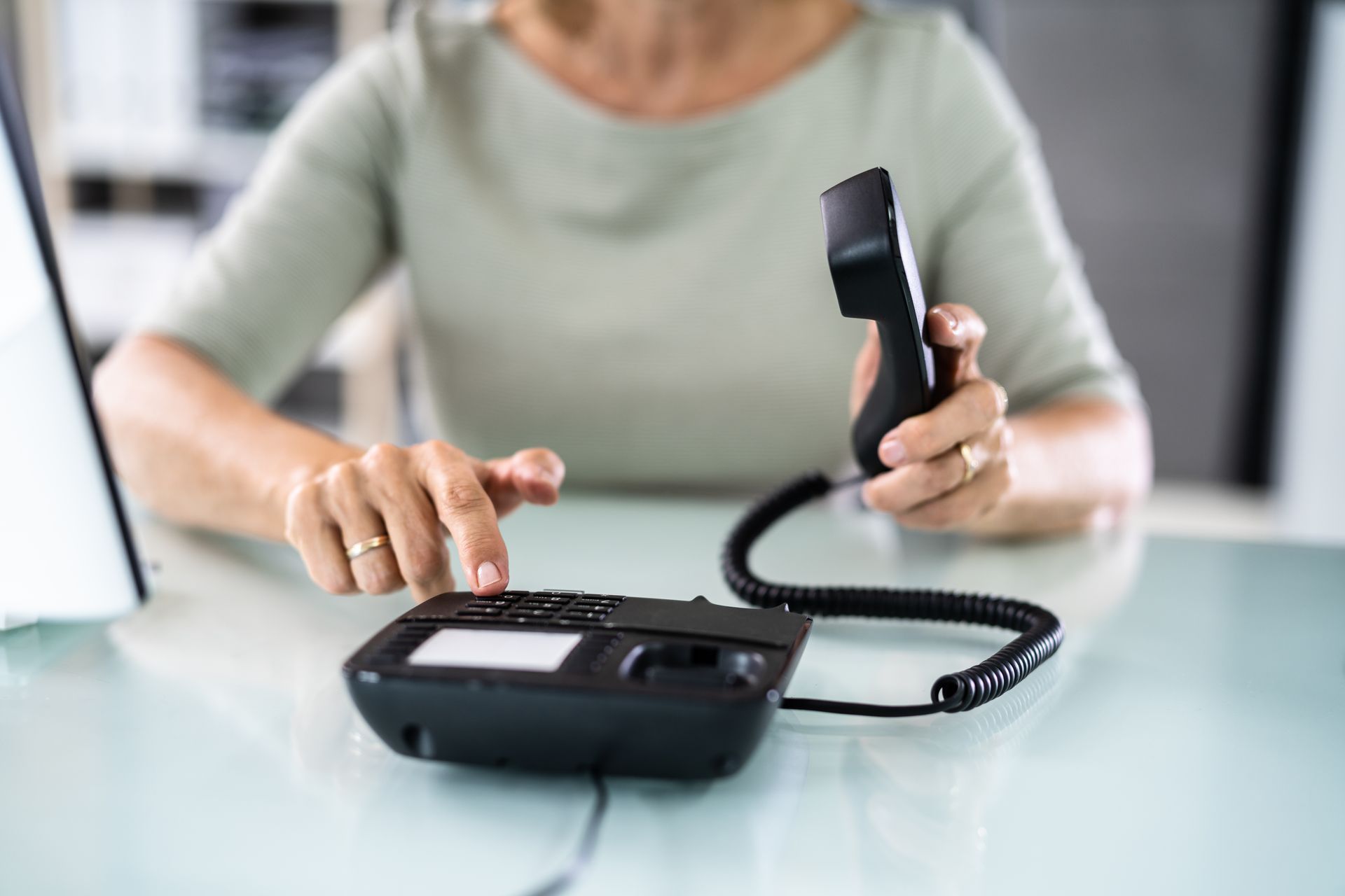 Woman at desk holding phone receiver, dialing numbers.
