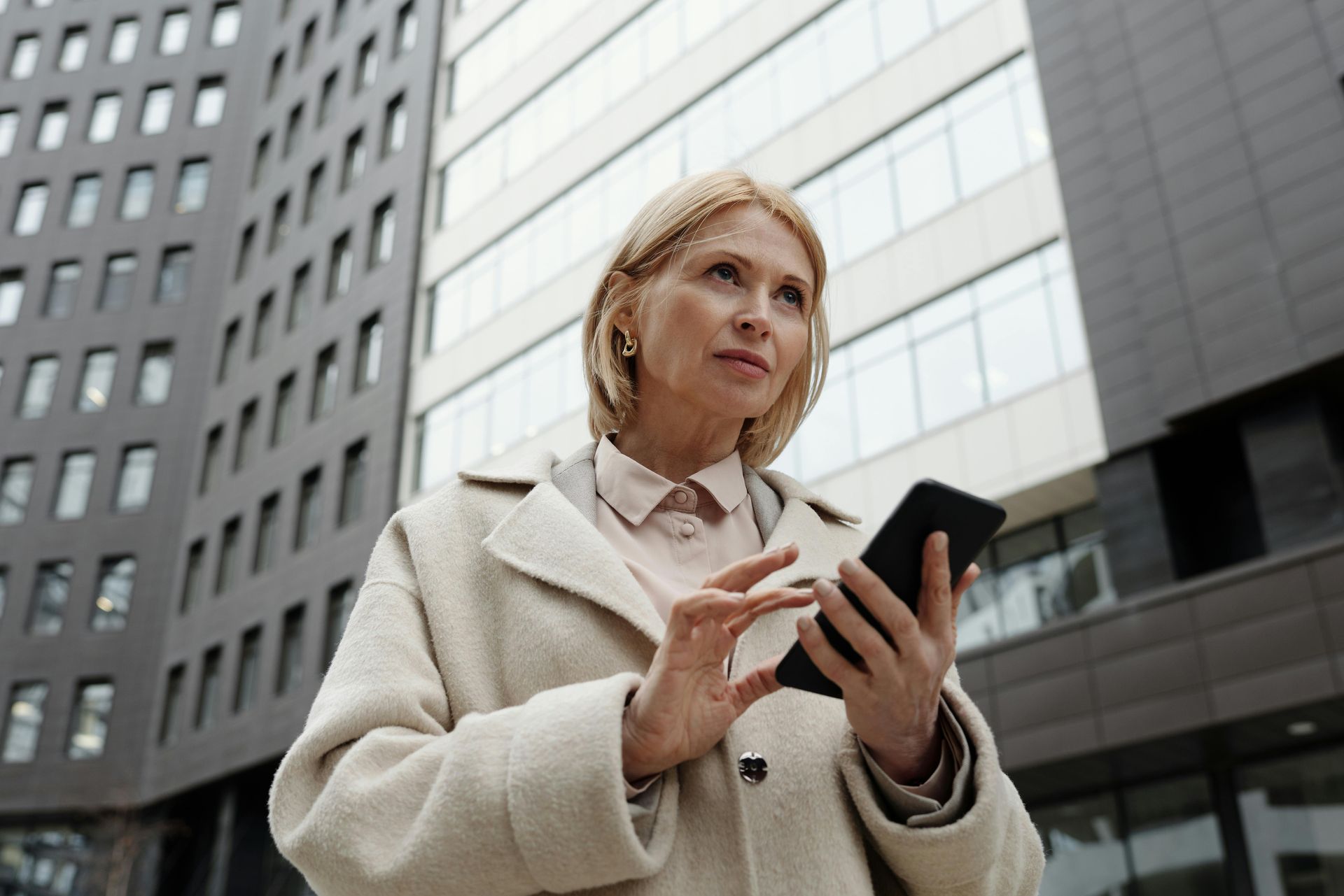 Woman in coat using a phone outside a modern building.