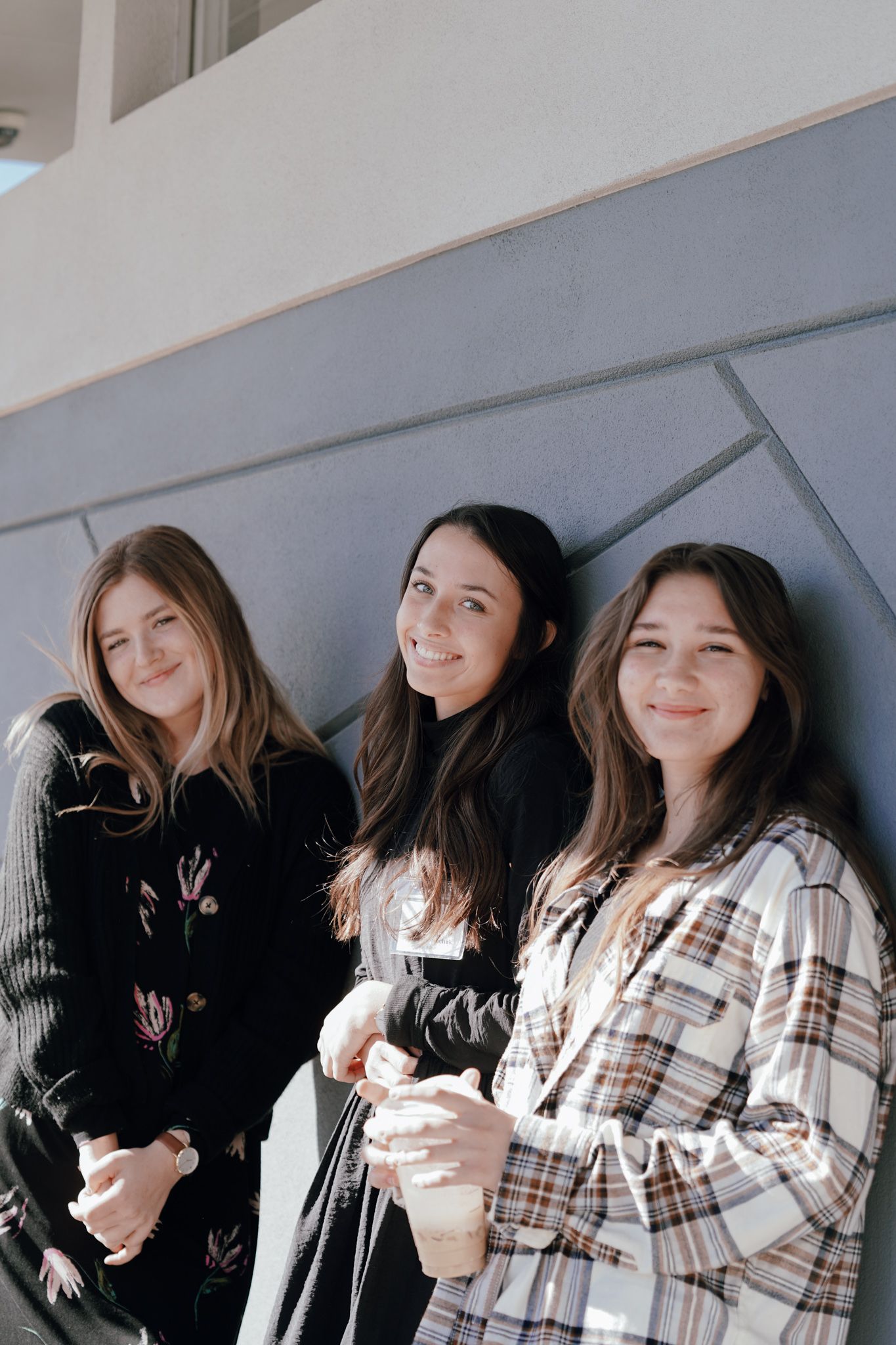 Three young women are standing next to each other in front of a wall.