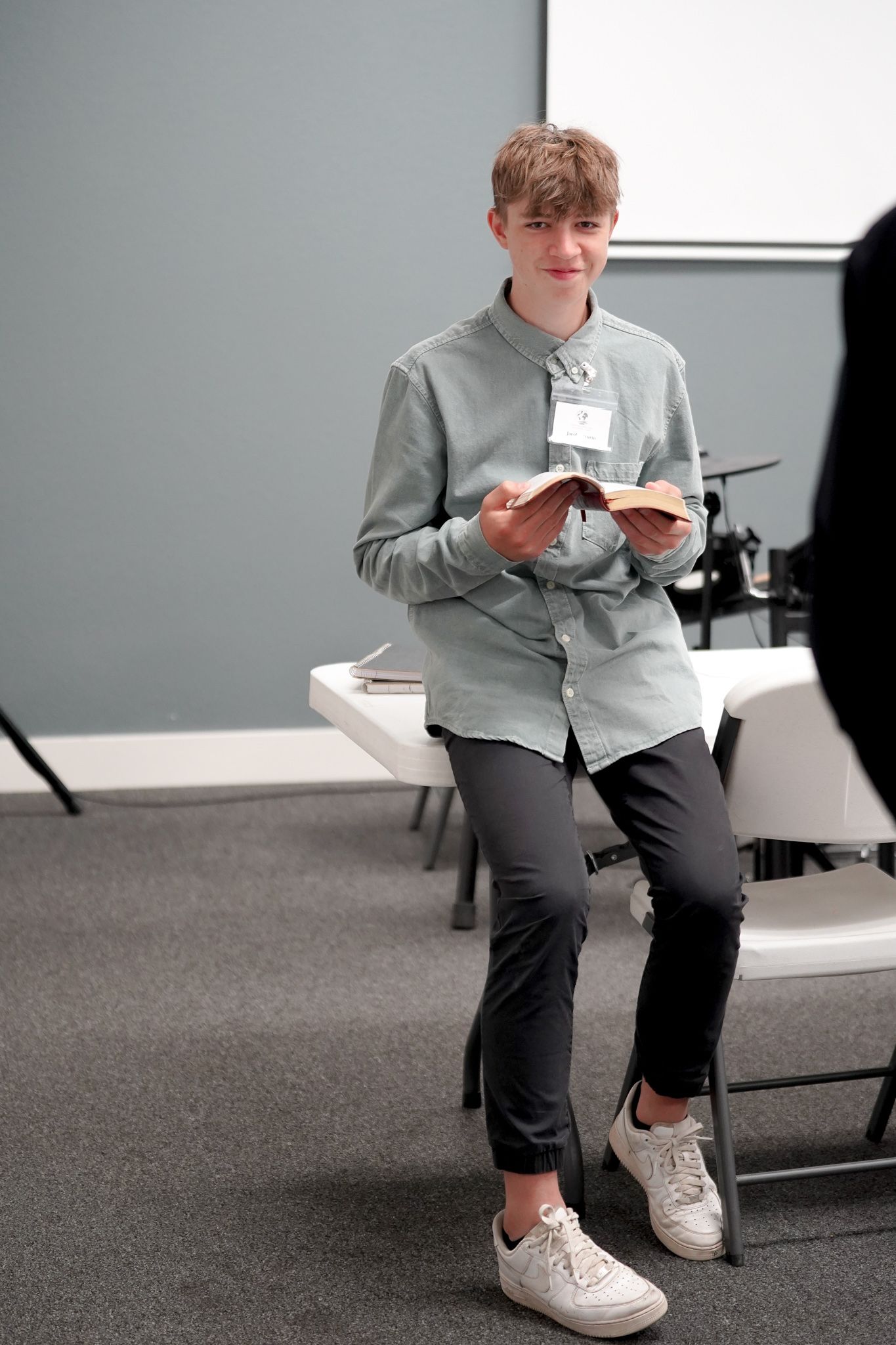 A young man is sitting in a chair reading a book.