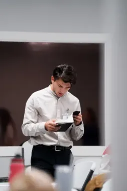 A man is standing in front of a window looking at his cell phone.