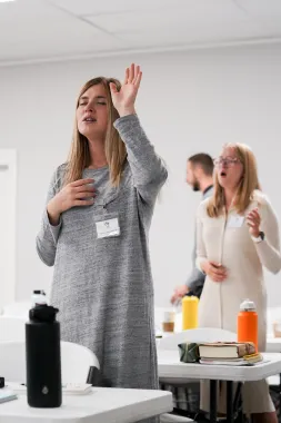 A woman is standing in front of a table with her hand up in the air.