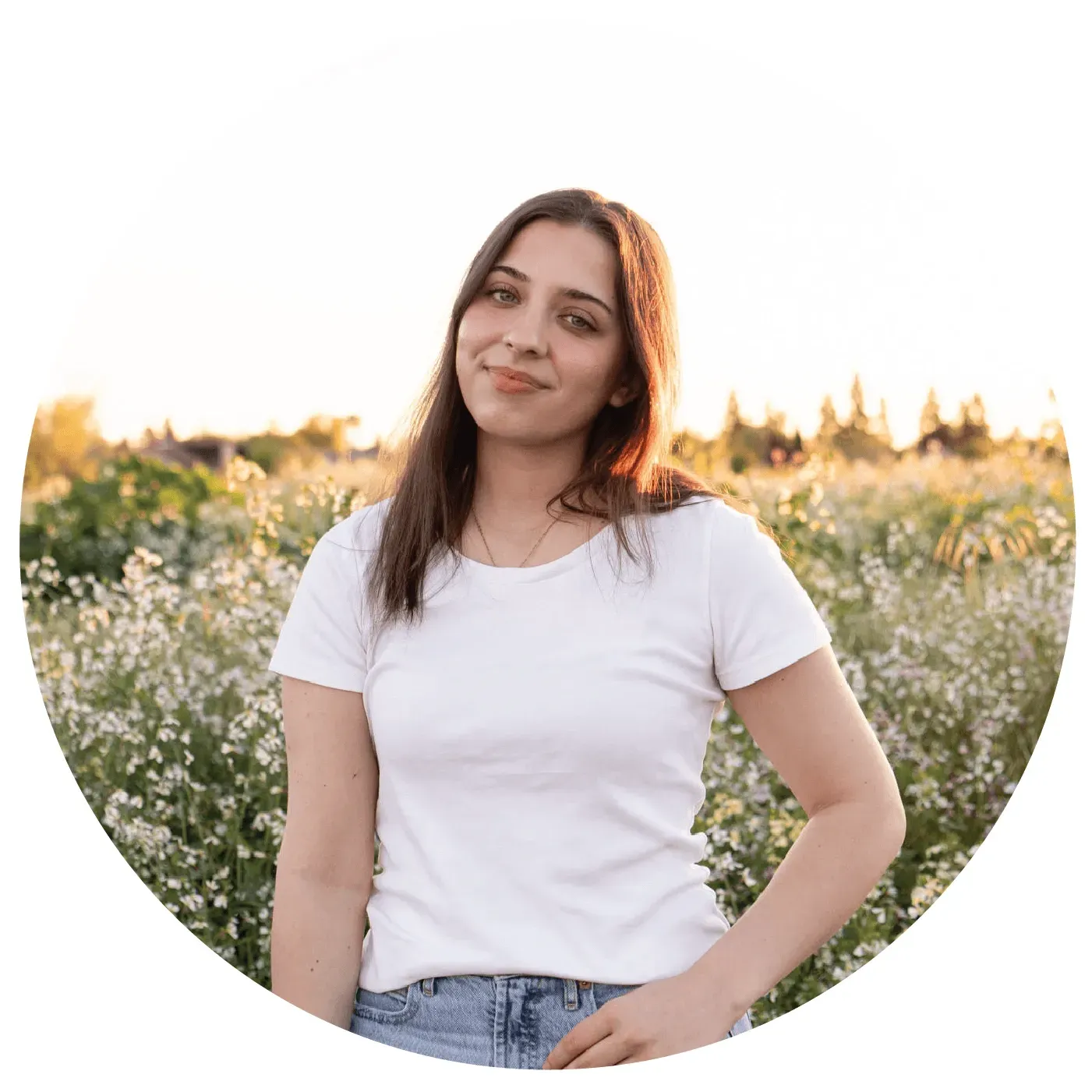 A woman in a white shirt and jeans is standing in a field of flowers.